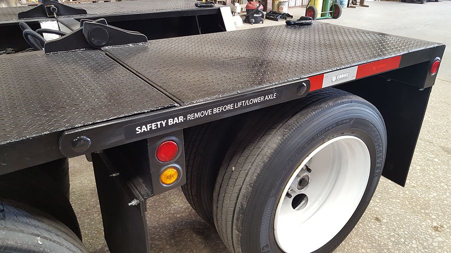 Flip-axle safety bar decal on the rear deck of a lowboy trailer